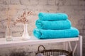 Rack with a stack of three color turquoise towels and baskets with clean white towels and toilet decor near brick wall. Shelf with Royalty Free Stock Photo