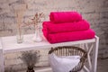 Rack with a stack of three crimson color towels and baskets with clean white towels and toilet decor near a brick wall. Shelf with Royalty Free Stock Photo