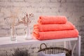 Rack with a stack of three peach color towels and baskets with clean white towels and toilet decor near a brick wall. Shelf with Royalty Free Stock Photo