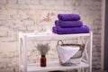 Rack with a stack of three purple color towels and baskets with clean white towels and toilet decor near a brick wall. Shelf with Royalty Free Stock Photo