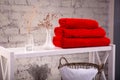 Rack with a stack of three red color towels and baskets with clean white towels and toilet decor near a brick wall. Shelf with Royalty Free Stock Photo