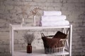 Rack with a stack of three white color towels and baskets with clean brown towels and toilet decor near a brick wall. Shelf with Royalty Free Stock Photo