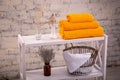 Rack with a stack of three yellow color towels and baskets with clean white towels and toilet decor near a brick wall. Shelf with Royalty Free Stock Photo