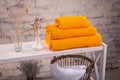 Rack with a stack of three yellow color towels and baskets with clean white towels and toilet decor near a brick wall. Shelf with Royalty Free Stock Photo