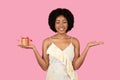 Radiant African American woman with curly hair, smiling and balancing a small gift box with a red ribbon Royalty Free Stock Photo