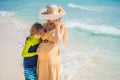 A radiant pregnant mother and her excited son share a tender moment on a serene, snow-white beach, celebrating