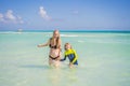 A radiant pregnant mother and her excited son share a tender moment on a serene, snow-white beach, celebrating