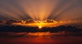 Radiant sunbeams pierce through dark clouds at sunset casting dramatic orange and yellow light Keywords: sunset Royalty Free Stock Photo