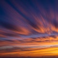 Radiant sunset sky displaying an array of elongated clouds in vibrant orange and Royalty Free Stock Photo
