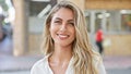 Radiant young blonde woman, exuding confidence with a sparkling smile, stands outdoors on a sunny city street, enjoying the urban Royalty Free Stock Photo