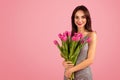 Radiant young woman with a captivating smile, holding a lush bouquet of pink tulips
