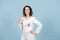 Radiantly smiling female nurse showing thumbs up. Over blue background