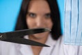 A young lady doctor is holding tailor`s scissors in front of her with a protective mask ready for cutting. The end of