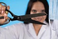 A young lady doctor is holding tailor`s scissors in front of her with a protective mask ready for cutting. The end of