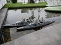A radio-controlled model of a warship with naval guns floats in an artificial reservoir, similar to a port on the street on a warm