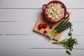 Radish, green onions, parsley, eggs salad in red bowl. Some fresh vegetables and greenery on kitchen chopping board on white Royalty Free Stock Photo