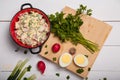 Radish, green onions, parsley, eggs salad in red bowl. Some vegetables  on chopping board on wooden background. Healthy eating Royalty Free Stock Photo