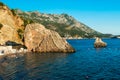 Beautiful puff rocks in sea near pebble public stone beach with resting peolpe at sunset. Rafailovici, Montenegro