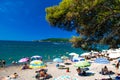 Resting people on public finely pebbly and sandy beach at a sunny summer day. Rafailovici, Montenegro