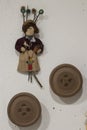 Rag doll hanging on a white wall with unfinished wooden figures with giant button shapes