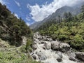 A raging and wild river flows between rocks in the valley with mountains beside it under a blue sky