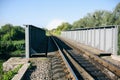 Rail tracks over the bridge in the green field. Railway transport industry. Empty road on summer day Royalty Free Stock Photo