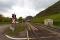 A railroad corssing with a red warning sign and warning lamp and a passenger train in background Royalty Free Stock Photo