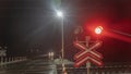 Railroad crossing with passing train by night. Train crossing gates closed on rural road at late evening. Drops of rain Royalty Free Stock Photo