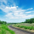 Railroad to green horizon and clouds in blue sky