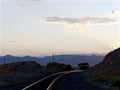 Railroad tracks curving around bend, illuminated by sunset, mountain range in background, vertical format