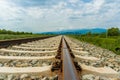 Railroad tracks leading to endless infinity. Meadow landscape and distant mountains. Royalty Free Stock Photo