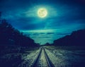 Railroad tracks through the woods at night. Beautiful sky and full moon above silhouettes of trees and railway. Serenity nature