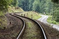 Railway curve and asphalt winding road in a green forest. Two communication and transport routes next to each other