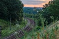 The railway line rails and electric poles and wires in the woodland in sunset time in summer