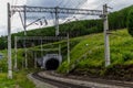 Railway, path with dark tunnel in green mountains hills forest, wire pillars, clouds