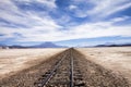 Railway in the salt desert near Uyuni, Bolivia with blue sky and mountains at horizon Royalty Free Stock Photo