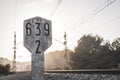 Railway traffic sign next to train tracks with kilometric numbering in concrete marker with sunset raylights