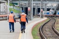 Railway workers on passenger platform. Technological buildings in the background