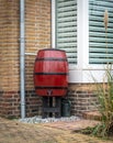 Red rain barrel with valve and watering can. Collecting rainwater by rerouting a section of a gutter downpipe. Royalty Free Stock Photo