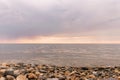 Rain clouds over the sea at sunset. Pebbles on the beach close-up, clouds colored the shades of pink and little waves on Royalty Free Stock Photo