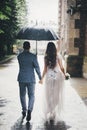 Rain drops on background of stylish bride and groom walking under umbrella and holding hands at old church in rain. Beautiful Royalty Free Stock Photo