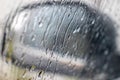 Rain drops rolling on window in storm, and a blurred black car side view mirror on a background, close up Royalty Free Stock Photo