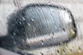 Rain drops rolling on window in storm, and a blurred black car side view mirror on a background, close up Royalty Free Stock Photo