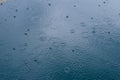 Rain drops on the surface of water in a puddle with graduated shade of black shadow and reflection of blue sky Royalty Free Stock Photo