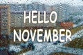 Rain falls on the surface of window panes with a cloudy background. Nature background with lettering Hello November. Royalty Free Stock Photo