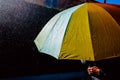 Rain falls on an umbrella among sun rays, dark background in black