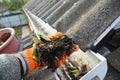 Rain Gutter Cleaning. Scooping leaves from gutter. Clean and Repair Rain Gutters and Downspout with roofer hands. Royalty Free Stock Photo