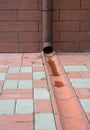 Rain gutter downspout pipe for roof runoff with open water drainage in the pavement. Gutter downspout pipe.