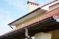 Rain gutters system on new house with chimney, red clay tiled roof and gable and valley type of roof construction