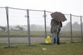In the rain. Man and woman standing under the umbrella behind the fence, landing field with planes on a background